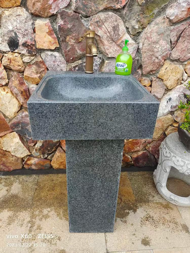 Installed rectangular stone pedestal basin against a stone wall